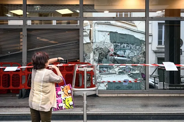 A woman passing by a damaged and looted shop in Lyon takes a picture of it