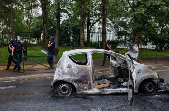 French police officers walk next to a burned out car in Nanterre