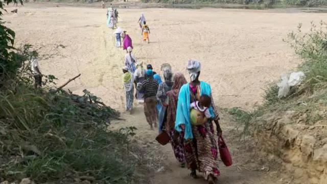 Women cross the dry bed of the White Volta river to their farms in Burkina Faso from Issakateng-Bausi, in Bawku, northern Ghana - December  2022