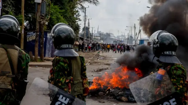 Police officers walking past a burning barricade during a mass protest over tax hikes