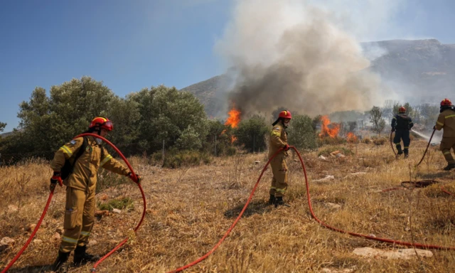 Firefighters try to extinguish a wildfire burning in Kouvaras, near Athens