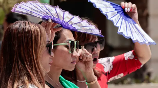 Tourists use fans to protect themself from the sun as they visit the coastal city of Valencia, southeastern Spain, 17 July 2023.