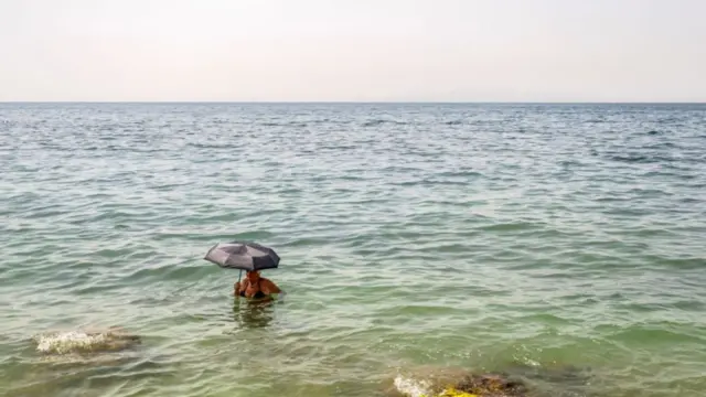 A woman holds an umbrella in the water at Alimos beach near Athens, on July 15, 2023,