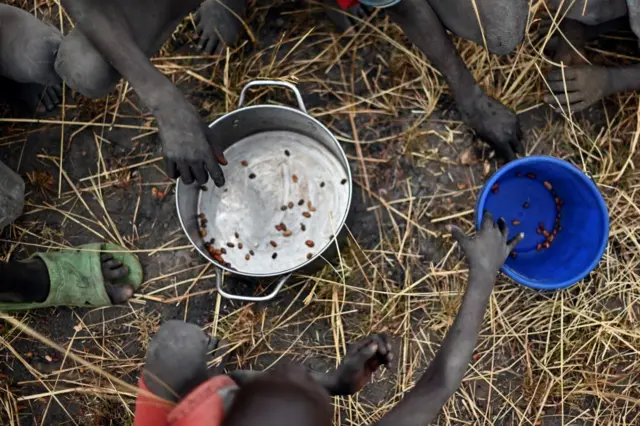 Children collect grain spilt on the field from gunny bags that ruptured upon ground impact following a food drop from a plane at a village in Ayod county, South Sudan, in 2020.