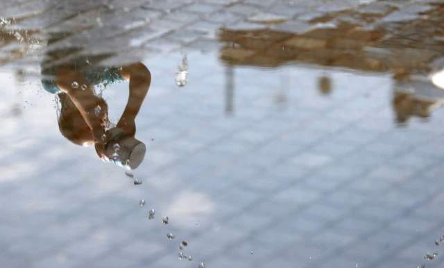 A girls is reflected in a puddle of water as she plays in a splash fountain in Madrid