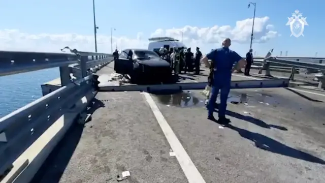 Russian investigators examine a destroyed car next to a heavily damaged section of bridge