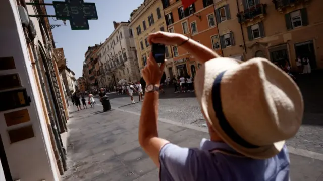 A man takes a picture of a sign that shows the temperature degree, near the Spanish Steps, Rome