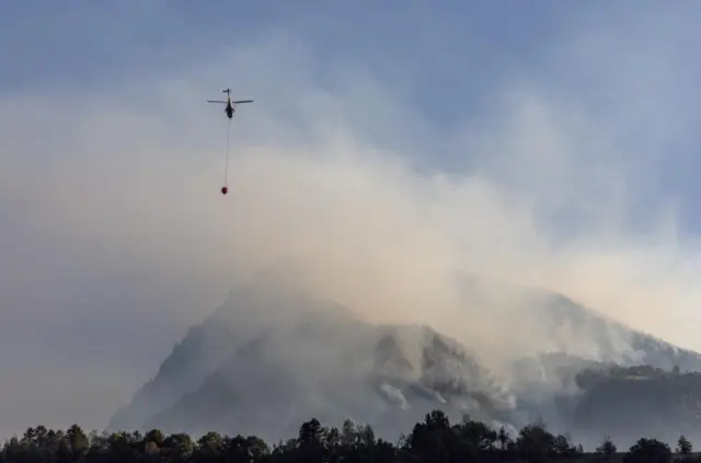 A helicopter carries water to a wildfire on the flank of a mountain in Bitsch