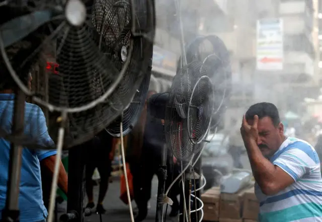 A man stands by fans spraying air mixed with water vapour deployed by donors to cool down pedestrians along a street in Iraq's capital Baghdad on June 30, 2021 amidst a severe heat wave.