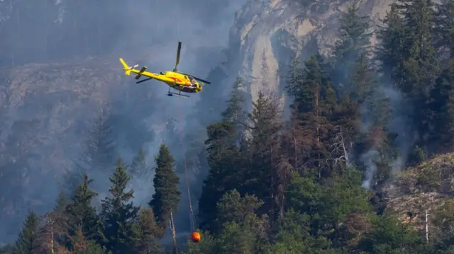 Helicopter carries water to a wildfire on the flank of a mountain in Bitsch near Brig, Switzerland