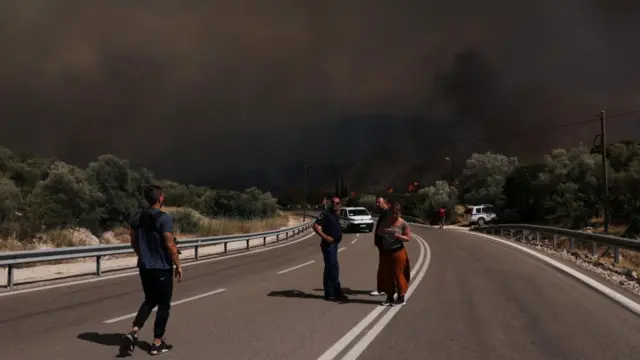 People are seen next to a wildfire burning near the village of Pournari, Greece,