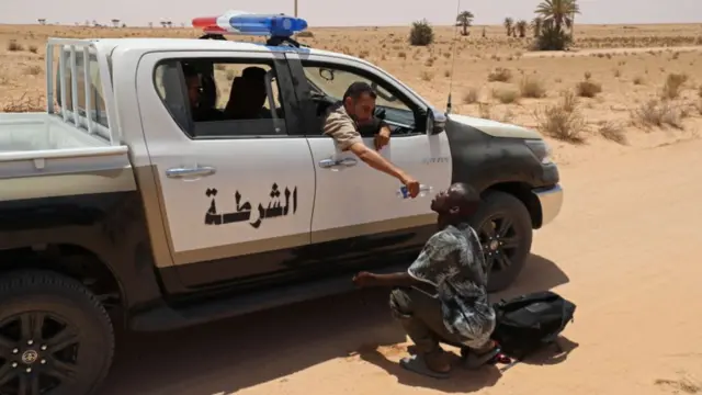 A Libyan border guard gives water to a migrant during a rescue operation in an uninhabited area near the border town of Al-Assah, on 16 July.