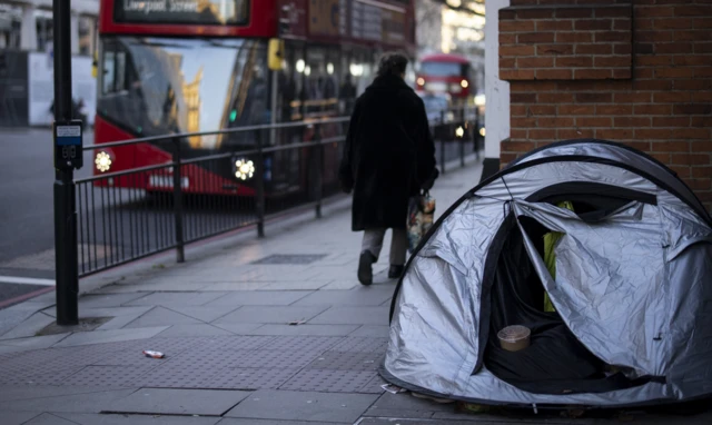 A person walks past a homeless person's tent in Belgravia, London