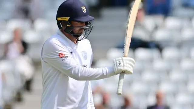 Ian Holland raises his bat after scoring fifty