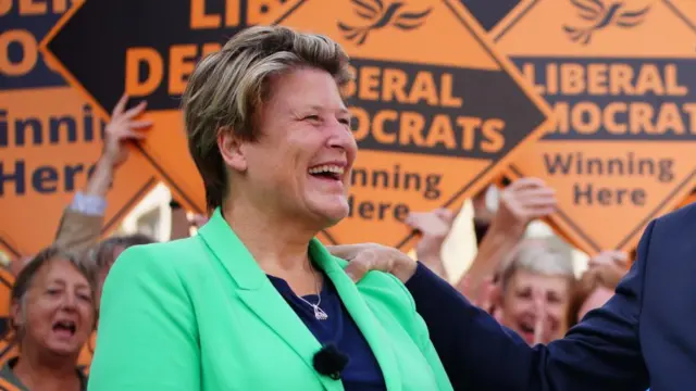 Sarah Dyke MP smiles in front of Liberal Democrat placards