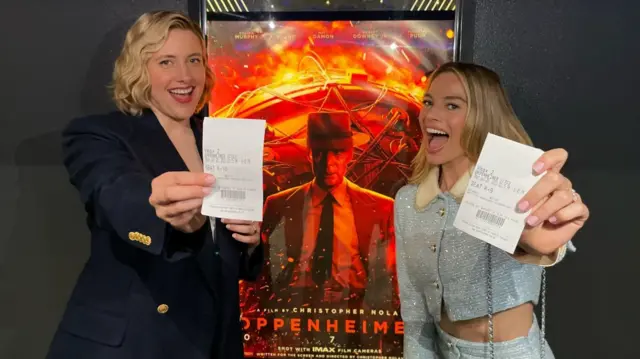 Barbie’s Margot Robbie and Greta Gerwig pose next to the Oppenheimer movie poster