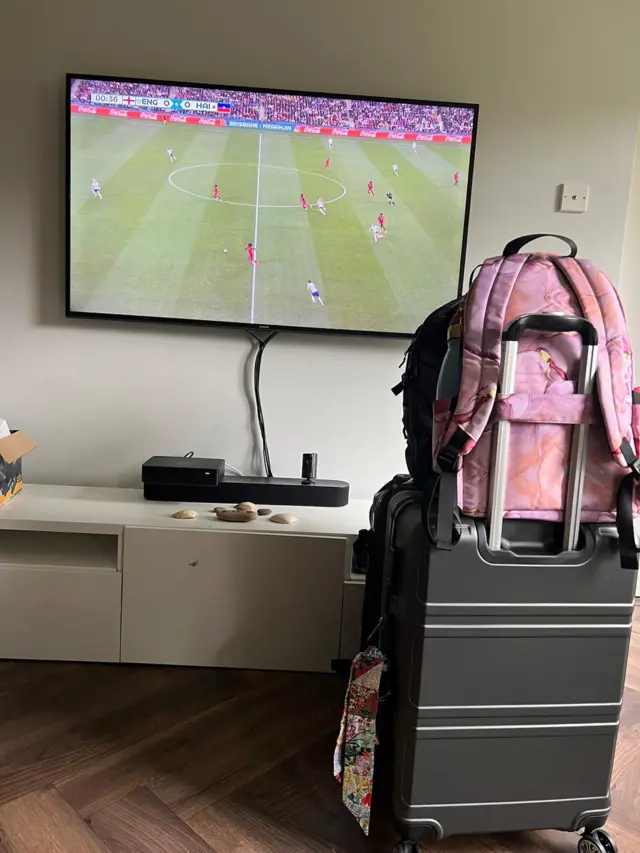 An England fan shows her suitcase ready for holiday in front of the match on tv.