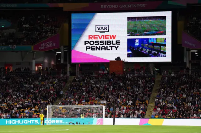 The stadium monitor shows a VAR check in progress.