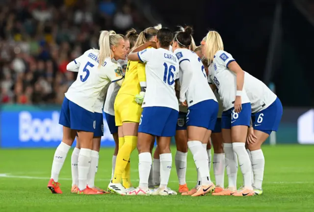 England players gather together in a huddle on the pitch.