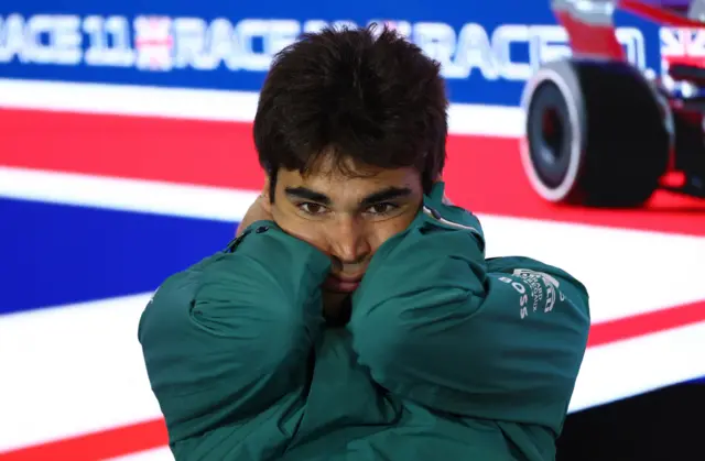 Lance Stroll wears a green Aston Martin jacket with his head in his hands