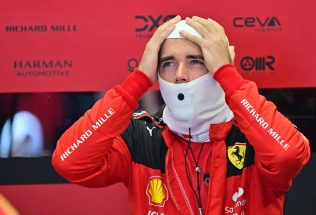 Charles Leclerc wears his red Ferrari race suit and as he puts on his fireproof headgear