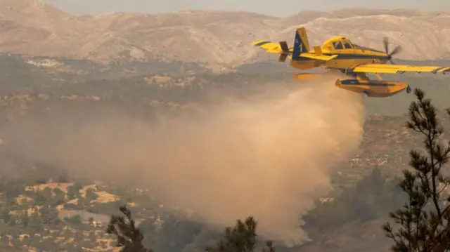 A firefighting aircraft drops water to extinguish a wildfire in Asklipio village