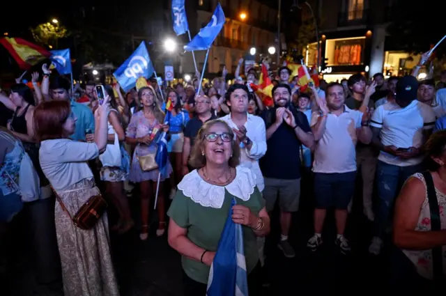 Supporters hold Spain's national flag as they wait for elections results in front of the headquarters of the leader and candidate of conservative Partido Popular (People's Party) Alberto Nunez Feijoo in Madrid on July 23, 2023,