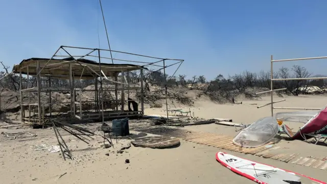 A burned out beach hut, with nearby damaged paddleboards and other watersports gear