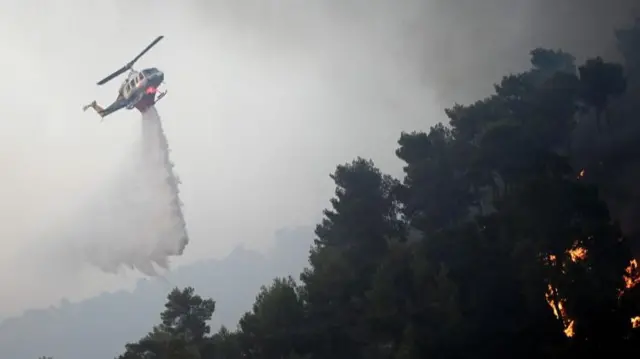 A firefighting helicopter drops water to extinguish a wildfire, in Diakopto, Egio, Greece, 24 July