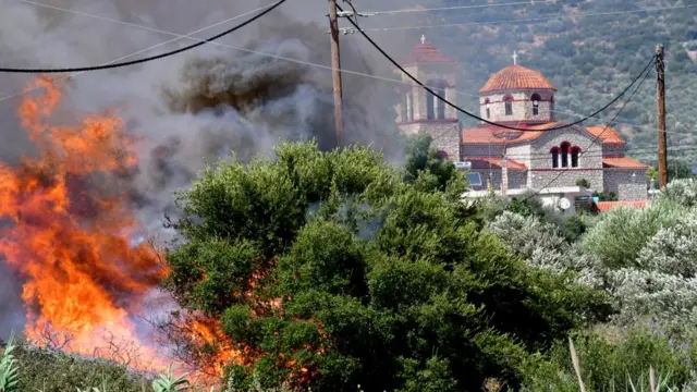 A wildfire burning with buildings in the background