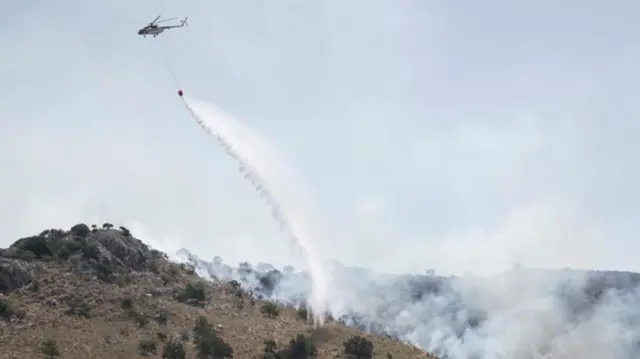 A firefighting helicopter drops water as wildfire burns near the village of Palia Perithia, on the island of Corfu