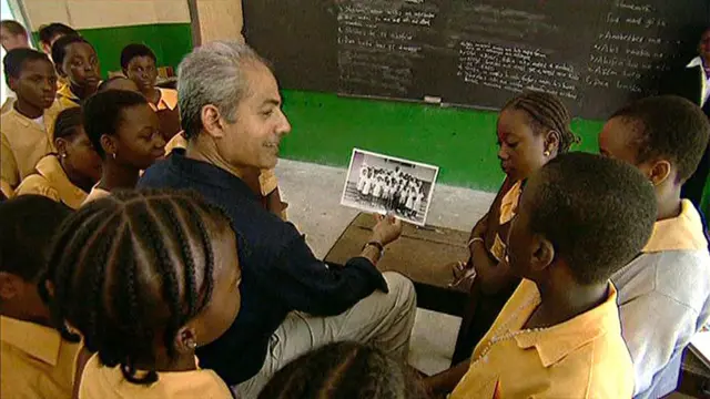 An adult George shows a black and white school photo to a class