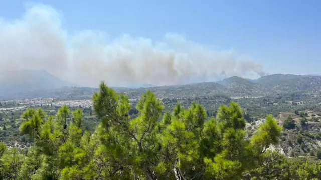 A very large smoke cloud billowing from a hill in the distance