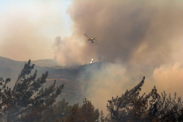 Firefighting aircrafts drop water to extinguish a wildfire in Asklipio village