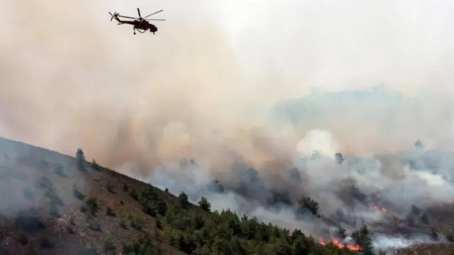 A firefighting helicopter makes a water drop as a wildfire burns near the village of Archangelos, on the island of Rhodes