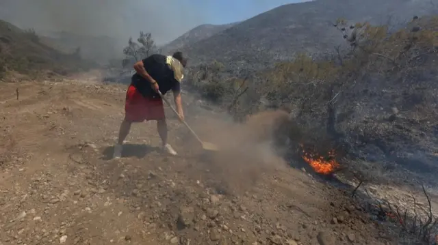 a man shovels dirt onto a small fire by a gravel road