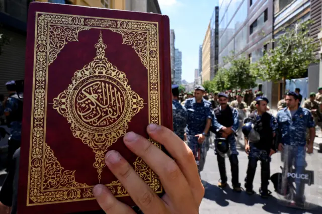 Lebanese police officers stand guard as a protester holds a copy of the Quran outside Sweden's embassy after Hezbollah leader called for protests outside mosques against the Koran desecration, in Beirut, Lebanon, 21 July 2023.