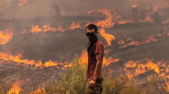 A man stands ready to fight flames as they engulf a hillside on July 27, 2023 in Apollana, Rhodes, Greece.