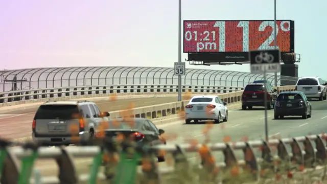 Cars on a freeway drive by a billboard showing 112F