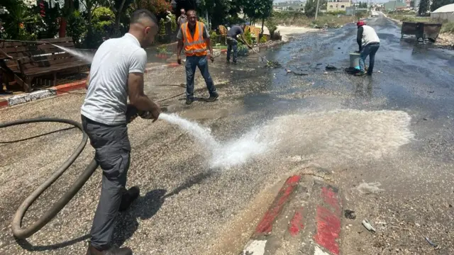 Municipal workers hose away the remains of burnt tyres