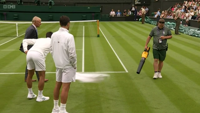 Novak Djokovic and Pedro Cachin watch on as water is removed from Centre Court