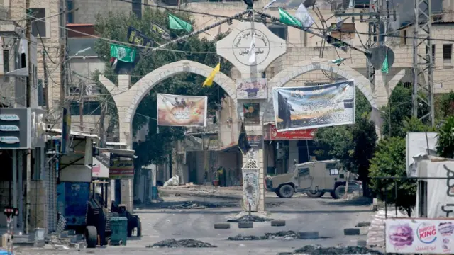 A view of debris at the entrance to the Jenin camp near an Israeli armoured vehicle (rear) during an Israeli military operation in Jenin, West Bank, on 3 July 2023.