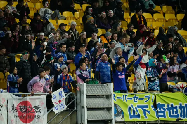 Japan fans cheer on their side from the stands with banners and flags.