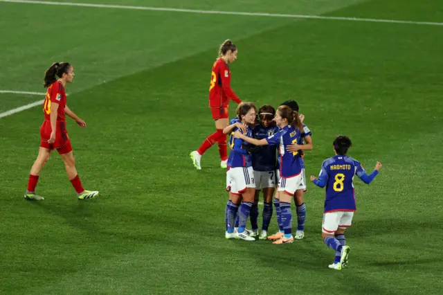 Japan players huddle together to celebrate with Spain players forlorn in the background.