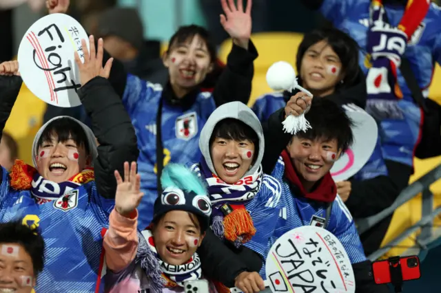 Japan fans wave at the camera and smile after their team record a famous win.