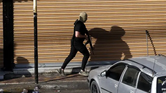 An armed Palestinian runs in a street during clashes with Israeli forces