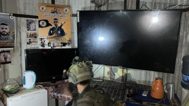 RC screens with posters of Palestinian militants on the wall behind and an Israeli soldier standing in front of them looking at the scene