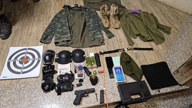 A collection of miltitary clothing and gear, including helmets, a pistol, camflage jhacket and a target to practice shooting at