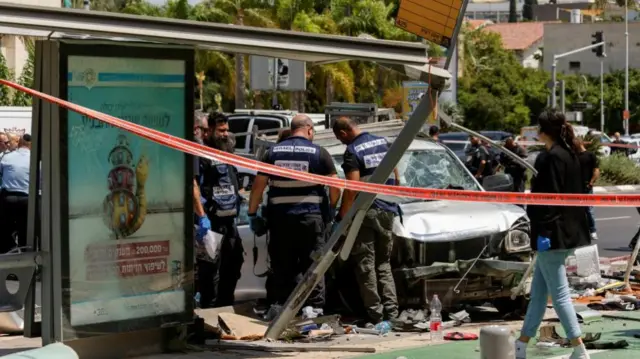 Israeli police work at the scene, the truck has heavily damaged windscreen and there is a damaged bus stop and lots of debris surrounding it