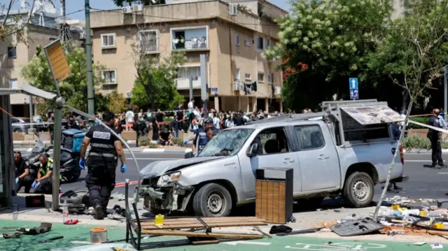 Israeli police work at the scene, the truck has heavily damaged windscreen and there is a damaged bus stop and lots of debris surrounding it